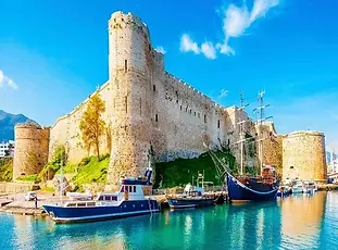 Scenic view of Kyrenia Harbour and castle in North Cyprus, surrounded by historic stone buildings, blue sea, and mountain backdrop under clear Mediterranean skies.
