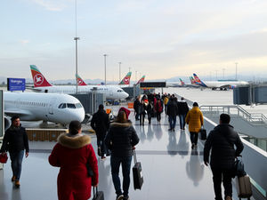 A photograph of Ercan International Airport terminal with multiple commercial aircraft parked and passengers moving through the arrivals/departures area in winter clothing, reflecting increased travel activity around the year-end holiday period.