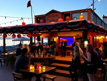 A lively beach-front pub in the Kyrenia (Girne) district of Northern Cyprus, decked in orange and black Halloween bunting, with live music on a small stage, costumed guests holding cocktails and enjoying the warm Mediterranean evening air.