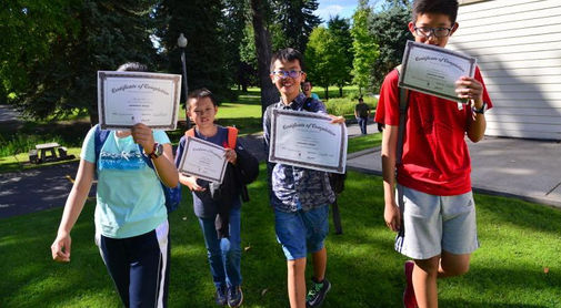 Smiling children hold Certificates of Completion outdoors
