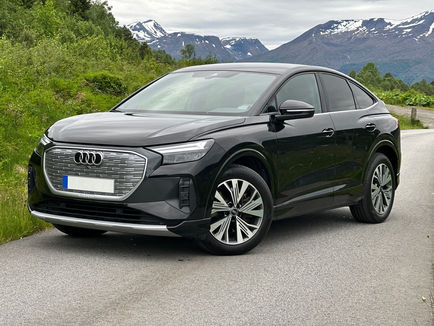 Audi Q4 Sportback 50 e-tron quattro i svart lack fotograferad snett framifrån med coupéformad SUV-profil och Audis Singleframe-front.