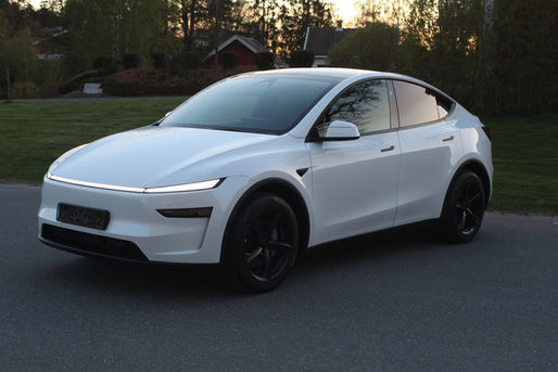 Vit Tesla Model Y Long Range AWD Juniper fotograferad snett framifrån i kvällsljus med ny ljuslist och svarta fälgar.