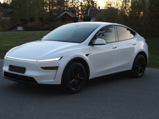 Vit Tesla Model Y Long Range AWD Juniper fotograferad snett framifrån i kvällsljus med ny ljuslist och svarta fälgar.