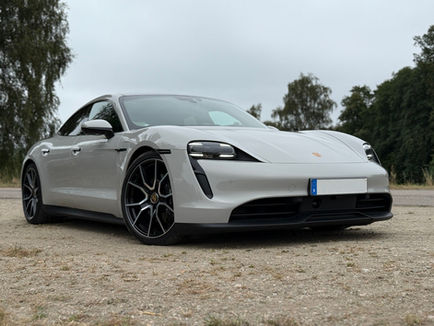 Ljusgrå Porsche Taycan 2023 fotograferad snett framifrån på landsväg med svarta detaljer, 21-tums RS Spyder-fälgar och låg fyrdörrars sportprofil.