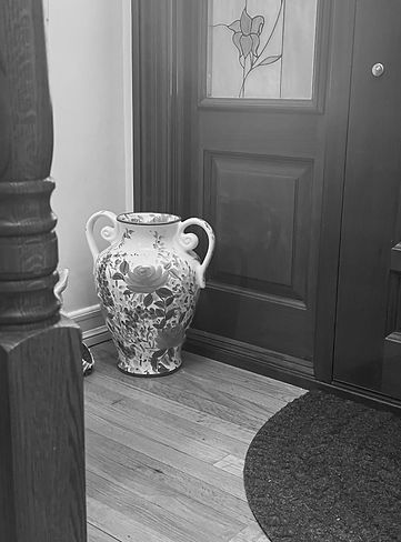 Black and white photograph of a staircase with a vase, rug, and door visible
