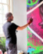 A man is spray painting a graffiti wall with shades of pink and green on a bar wall