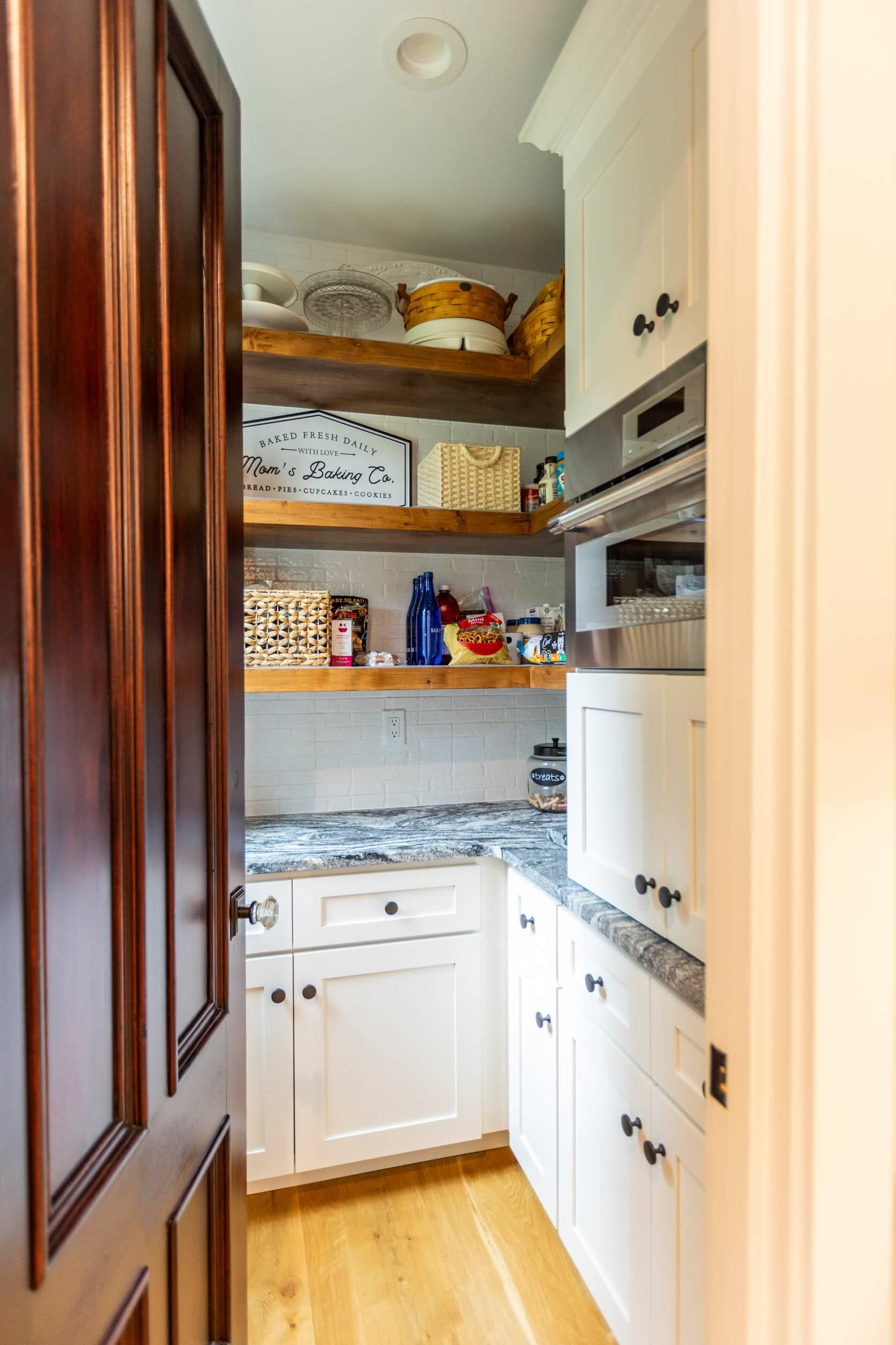 Small pantry with wooden shelves and white cabinets.