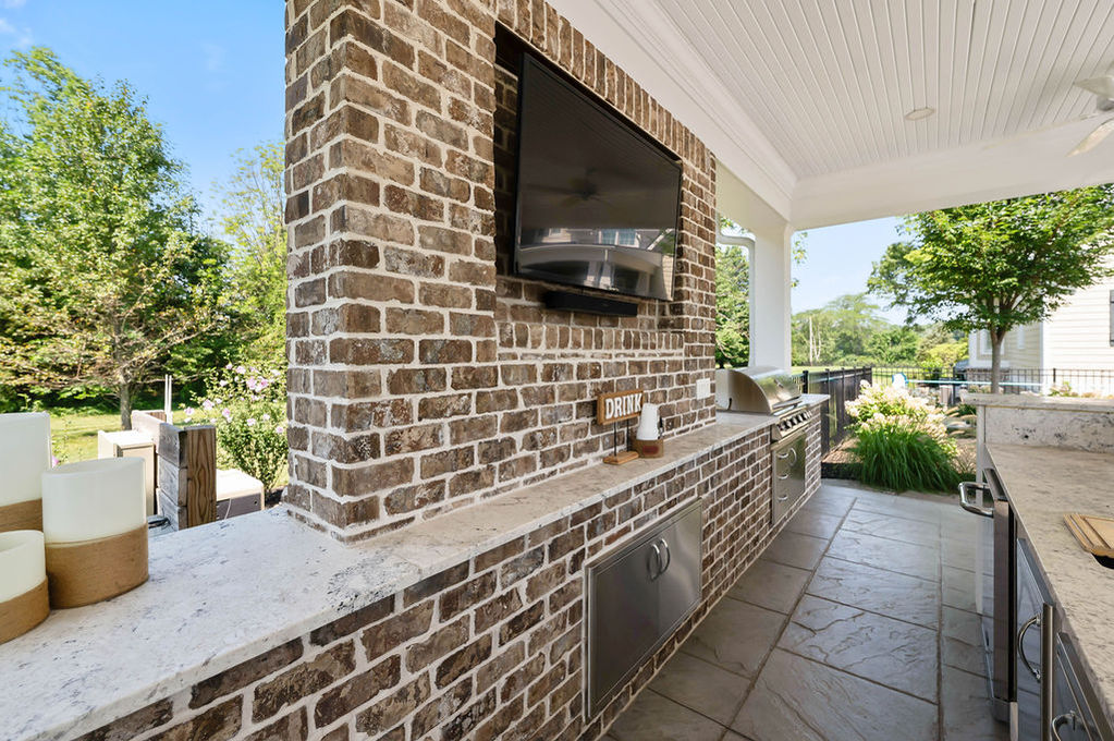 Outdoor kitchen with brick design and mounted TV.
