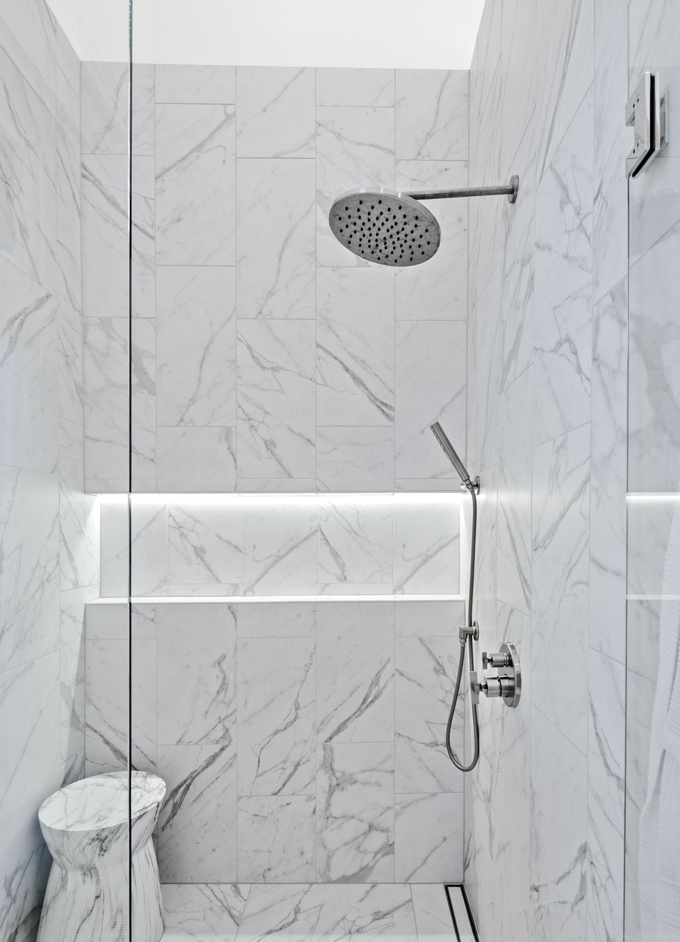 Marble shower with modern rain showerhead and lighting.