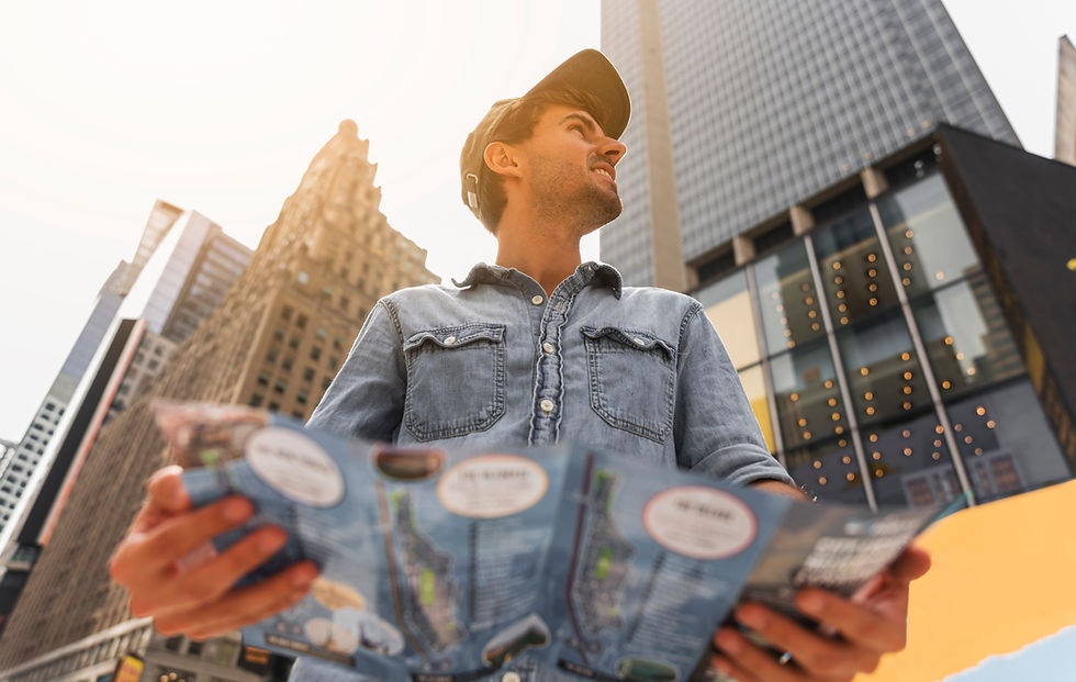 A person in a denim shirt and cap holds a map, looking up in a city with tall buildings and a bright sky. Mood is curious and explorative.