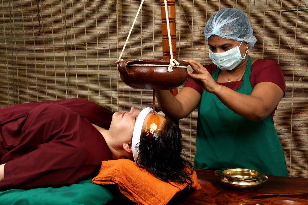 Therapist pouring oil onto a woman's forehead during a treatment