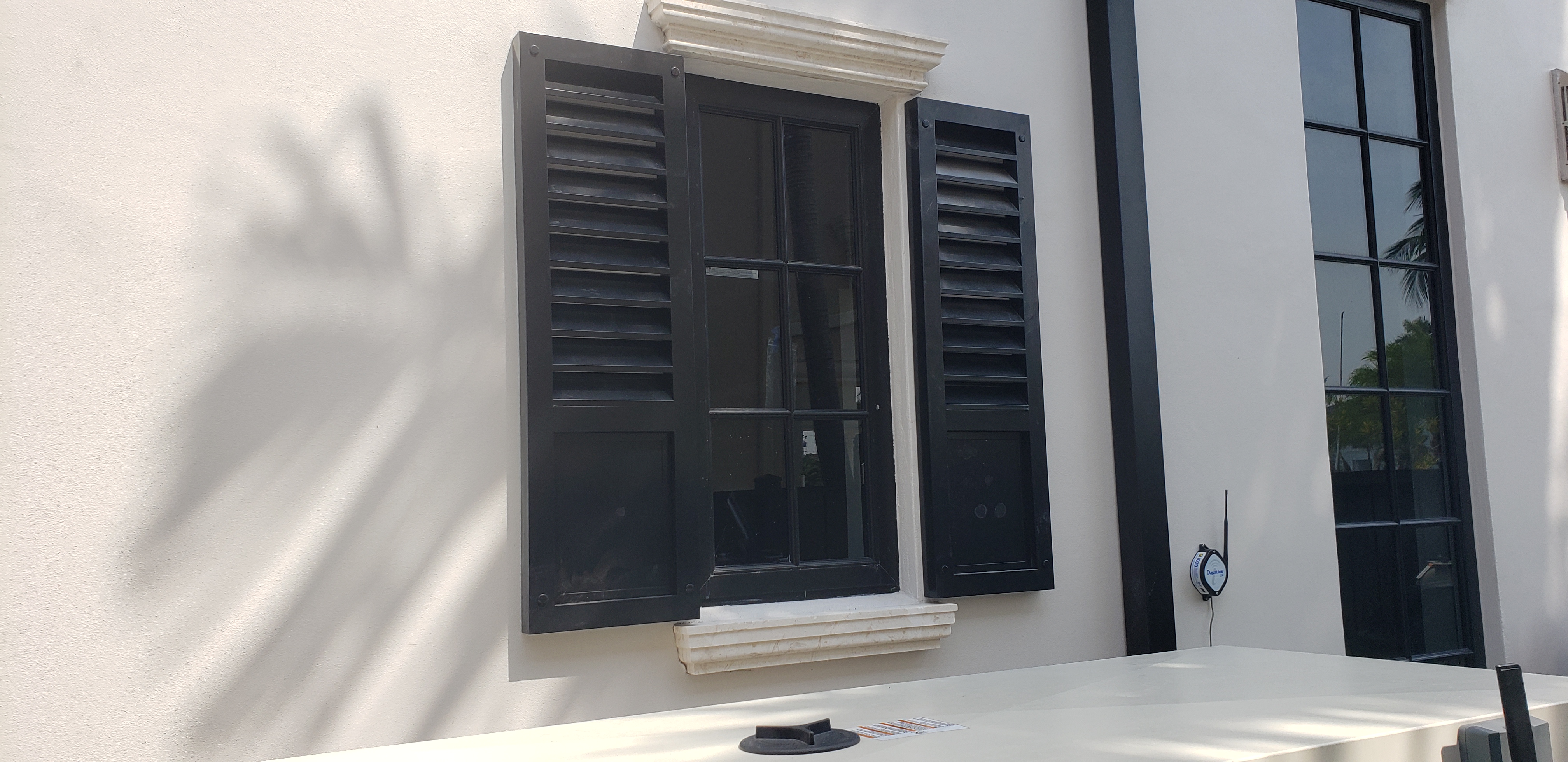 Black Bahama shutters flanking a window, coastal residence