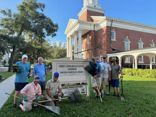 Men pose with lawn tools after cleaning up hurricane debris in front of the church.