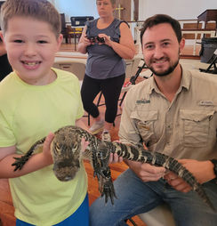A boy holding a baby alligator with help from a man