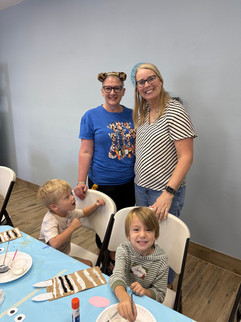 two women and two young children who are making paper bag puppets that look like zebras