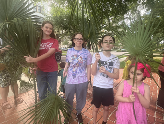 two teens and two children holding large palm fronds outside of the church