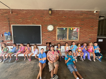 A group of youth and children sitting on white benches and on the ground.