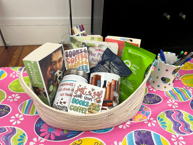 A basket with books, a coffee mug, a tumbler, coffee, chocolate covered espresso beans, and magnets. one magnet says "just a girl who loves books and coffee"