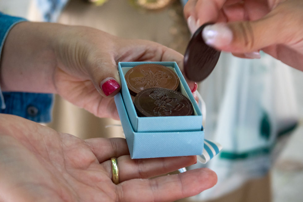 A small blue gift box filled with handcrafted chocolate medallions is shared between guests during a Paris shopping tour. One person lifts a chocolate coin from the box, revealing an elegant sweet treat inspired by French traditions.