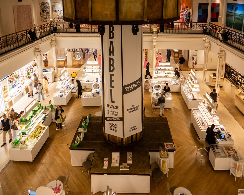 Interior of a historic Paris department store featuring elegant balconies, polished wood floors, and beautifully arranged beauty and fragrance counters. Shoppers browse luxury products beneath a large central display, blending classic architecture with modern Parisian retail.