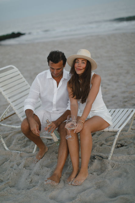 a man and a woman sit on a beach holding wine glasses