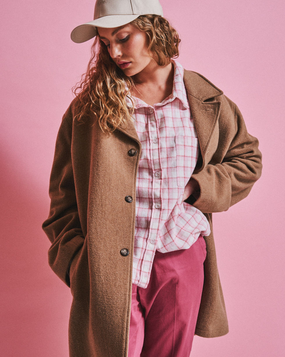 Model in a tan coat and pink check shirt against a pink studio backdrop, Melbourne, Australia; styling by Tamarra McNaught, founder of TITO STYLE.