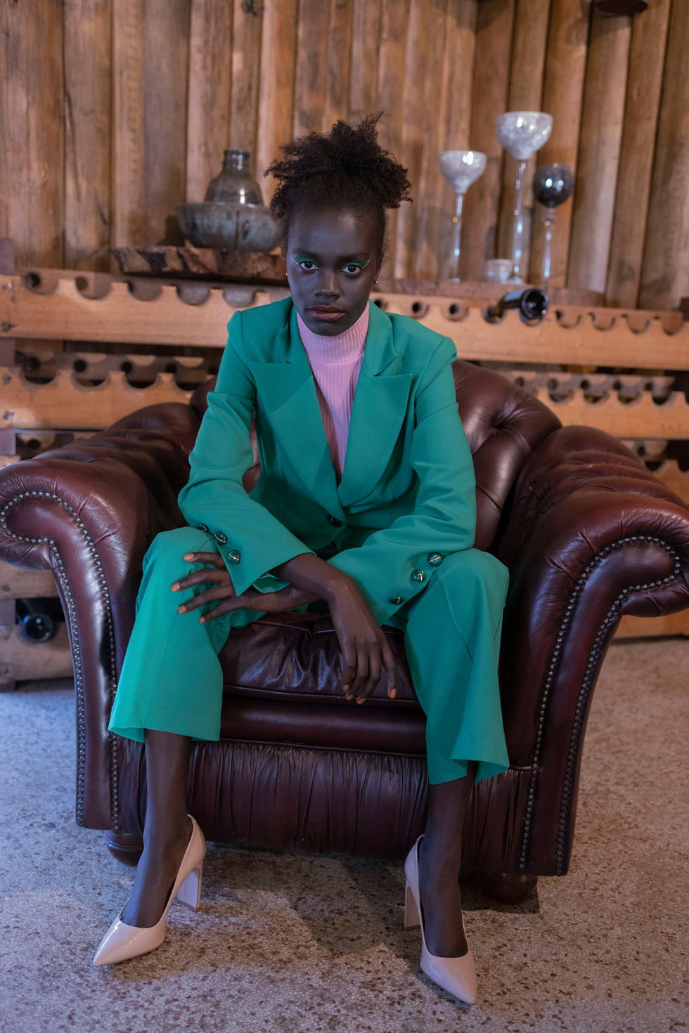 An emerald green suit, seated in a leather armchair in the estate interior. A Moss & Spy suit, with creative direction and styling by Tamarra McNaught, founder of TITO STYLE, at Riverlea Estate, Warrandyte, Victoria, Australia.