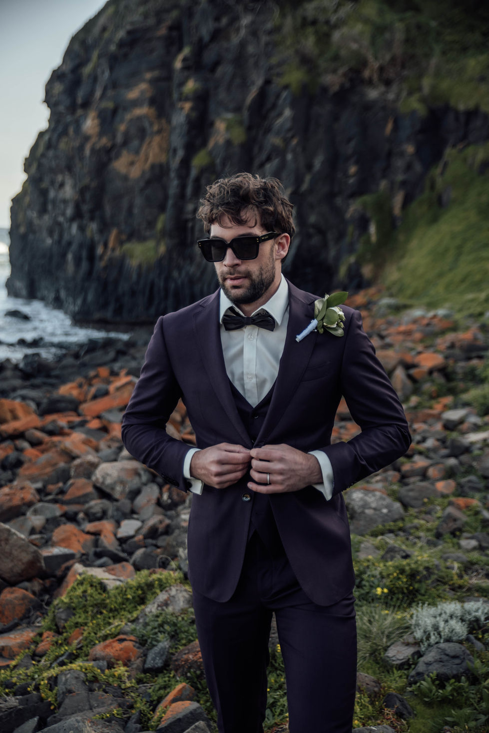 A groom alone in a dark suit and sunglasses. Menswear by YSG Tailors with sunglasses by Gucci, styling by Tamarra McNaught, founder of TITO STYLE, at Cairn Beach, Australia.