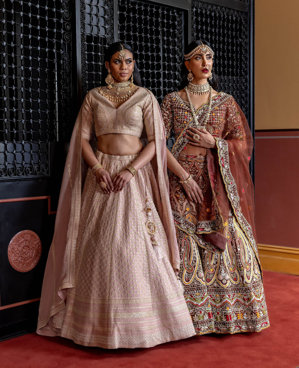 Two models in blush and maroon bridal lehengas by Rajashree Bridal Studio against a heritage screen at The Hotel Windsor, styled by TITO STYLE.