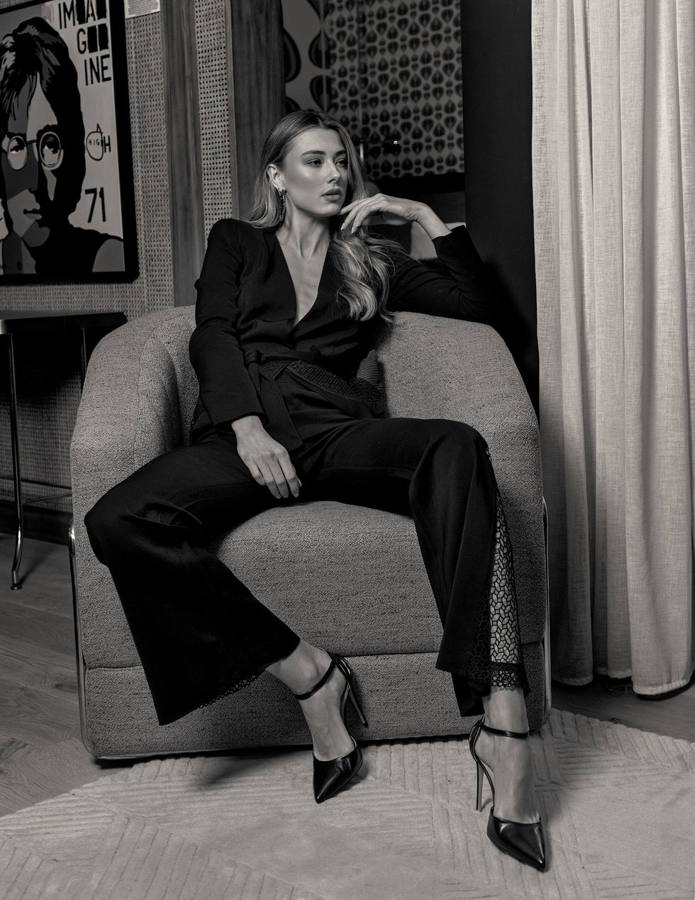 Black-and-white portrait of a model in a black tie-waist suit seated in an armchair, retro interior at Ovolo South Yarra, Melbourne, Australia; styling by Tamarra McNaught, founder of TITO STYLE.