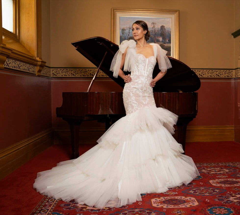 Bride in a Jullia Bridal lace mermaid gown with tulle shoulder bows beside a grand piano at The Hotel Windsor, Melbourne; creative direction and styling by Tamarra McNaught, founder of TITO STYLE.