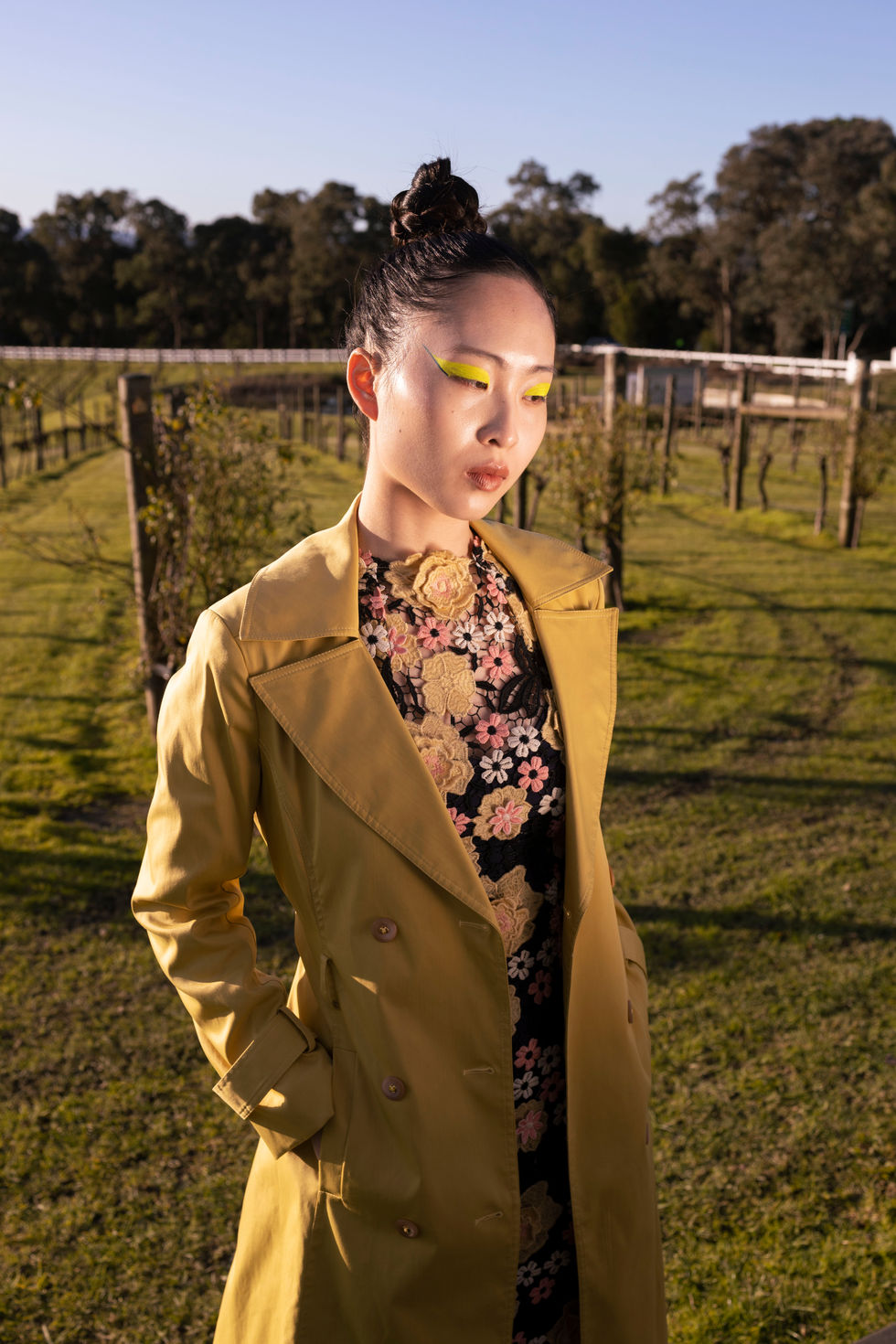 A tan trench-style coat worn over a printed dress in the vineyard. A Moss & Spy look, with creative direction and styling by Tamarra McNaught, founder of TITO STYLE, at Riverlea Estate, Warrandyte, Victoria, Australia.