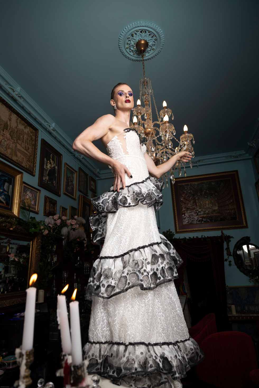 Adam Noviello beneath a chandelier in a tiered white and black gown by Paul McCann, editorial by TITO STYLE