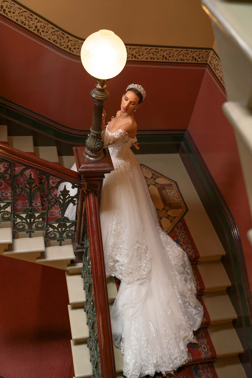 Bride in a Jullia Bridal lace ballgown beside an antique globe lamp on a sweeping staircase at The Hotel Windsor, Melbourne; creative direction and styling by Tamarra McNaught, founder of TITO STYLE.
