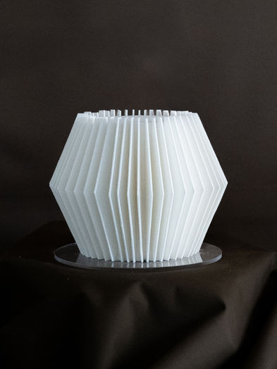 A three-tier all-white modern wedding cake from The Origami collection, featuring hand-cut geometric pleats and sharp architectural lines, displayed at a Brooklyn industrial venue.