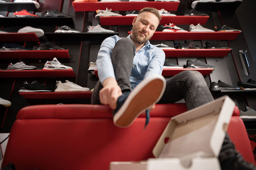 Bearded man chooses hiking shoes while sitting in fitting room of modern sports store