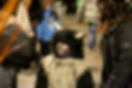Child in a furry costume with horns and painted face looks thoughtful. Crowded background with people in winter clothing. Cozy, festive mood.