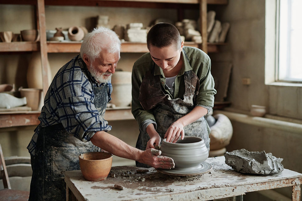 Young female potter making earthenware vase on pottery wheel with senior man helping her