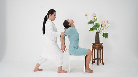 A woman sitting on a treatment chair in a room, receiving a stretching therapy session, with calming décor and plants around