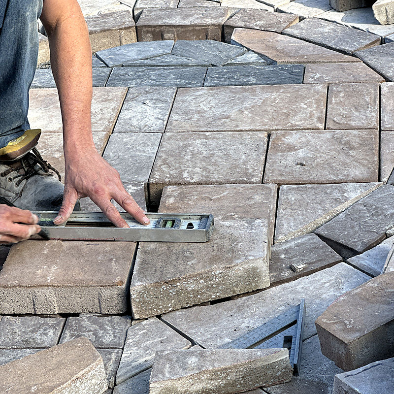 Worker using a level tool to align stone patio pavers.
