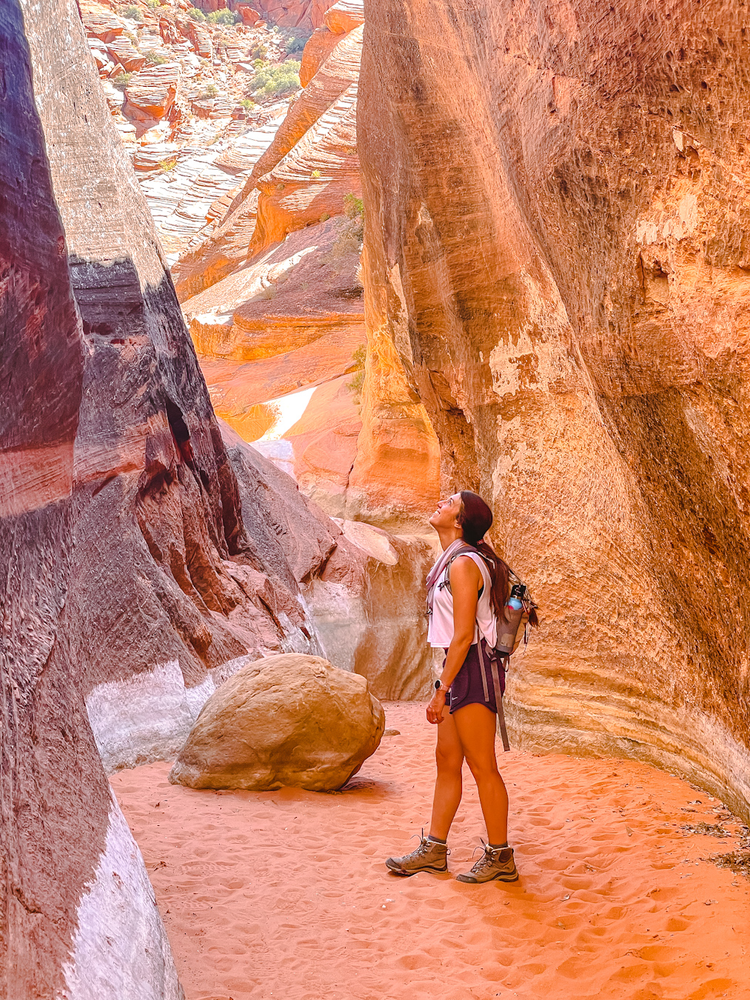 A woman stands inside of a sandy slot canyon