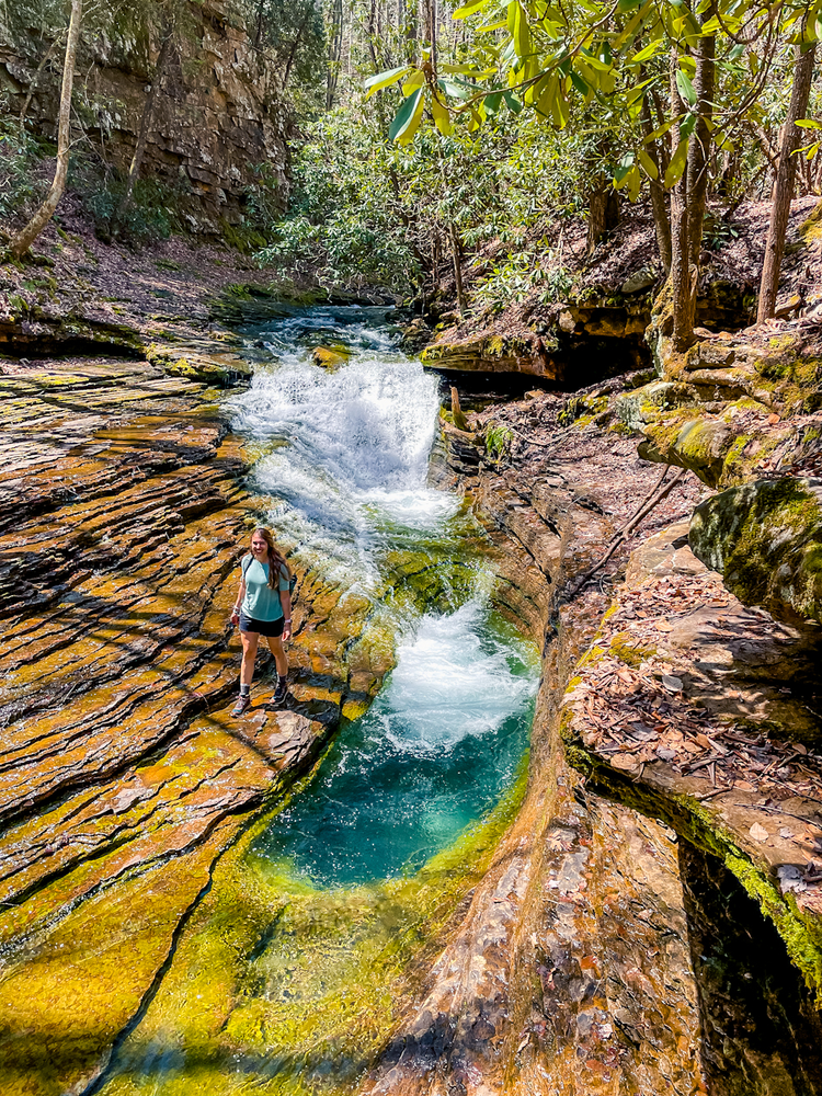 A girl stands near a natural water feature shaped like a bathtub