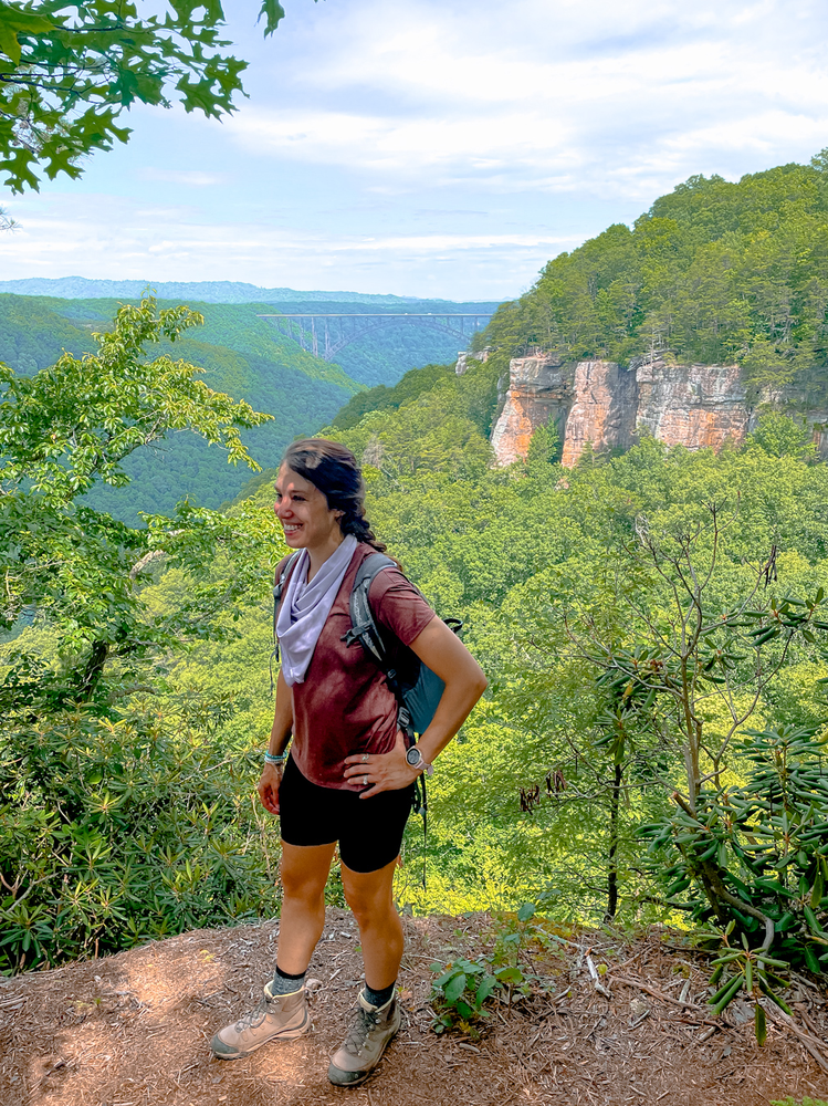 A girl standing near a ledge with a bridge and cliff in the background