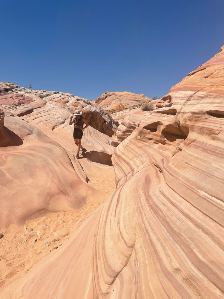 A woman stands in a small slot canyon with pink colored striations in the rock