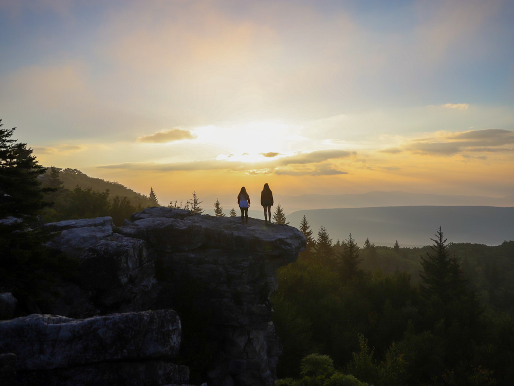 two girls stand on a rock overhand facing the sunrise