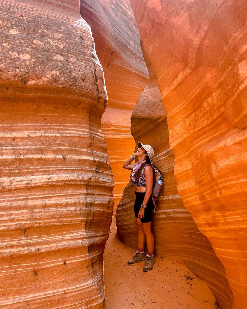 A woman can be seen standing inside of a slot canyon where there a stripes in the canyon walls