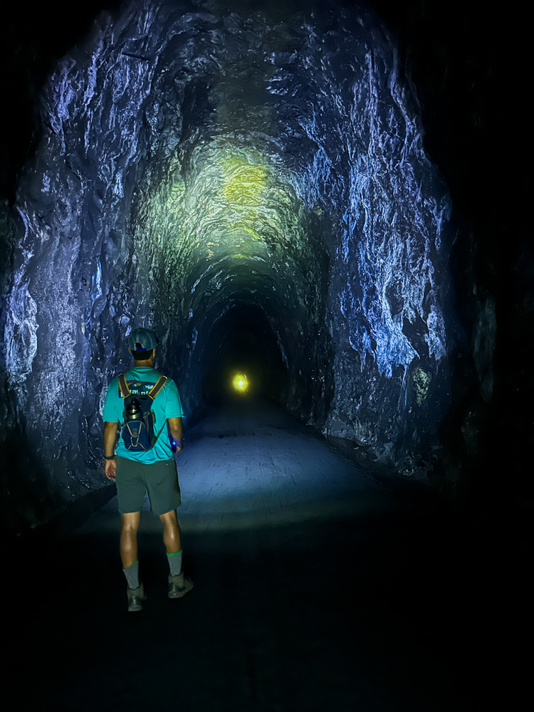 A man walks through a dark tunnel with a flashlight