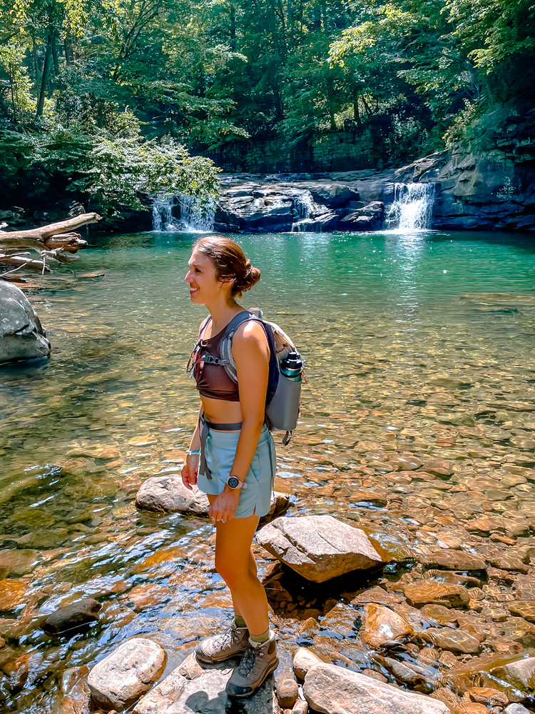 A girl standing in front of a waterfall and swimming hole