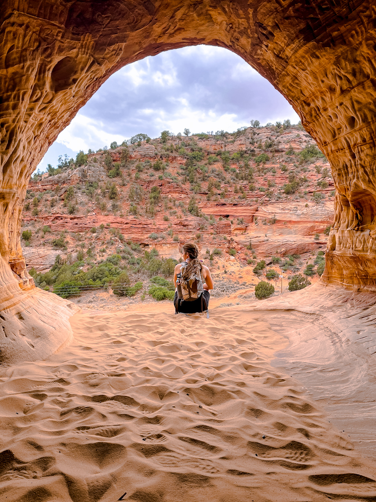 A woman can be seen sitting at the edge of an opening in a sandy cave