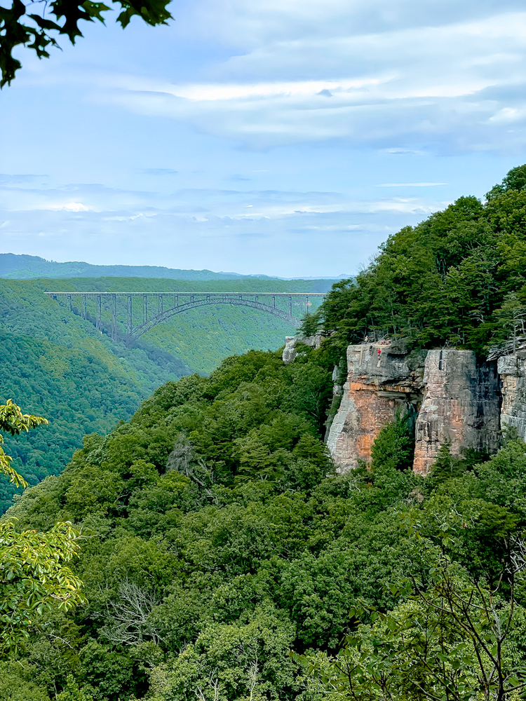 A bridge in the distance and climbers ascending a sheer cliff face